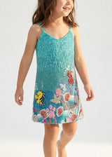 Child wearing a blue dress with ocean-themed designs on a white background