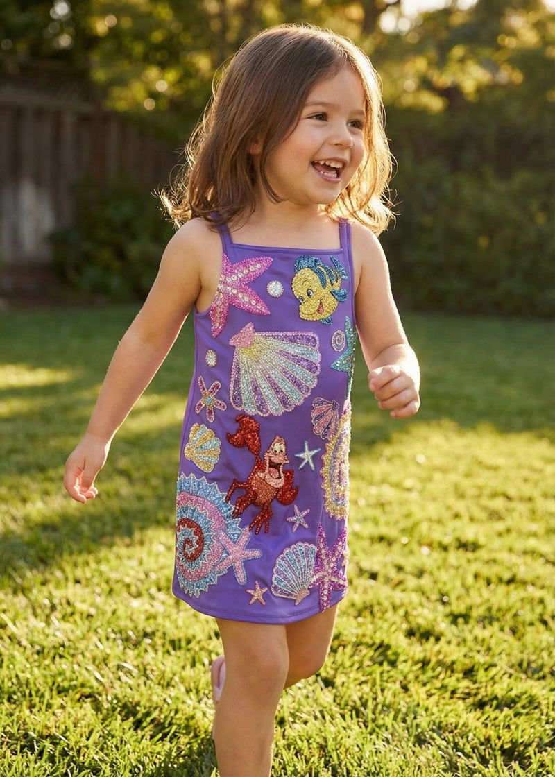 Child wearing a colorful dress with sea-themed designs outdoors on grass
