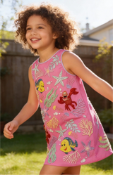 Child wearing a pink dress with colorful sea-themed designs outdoors.
