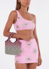 Woman wearing a pink outfit with decorative elements, holding a checkered bag.
