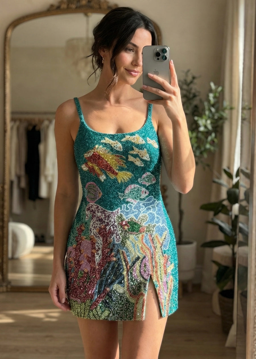 Woman taking a mirror selfie wearing a colorful sequin dress in a room with plants and a mirror.