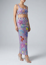 Woman wearing a colorful top and skirt with mermaid-themed designs on a gray background