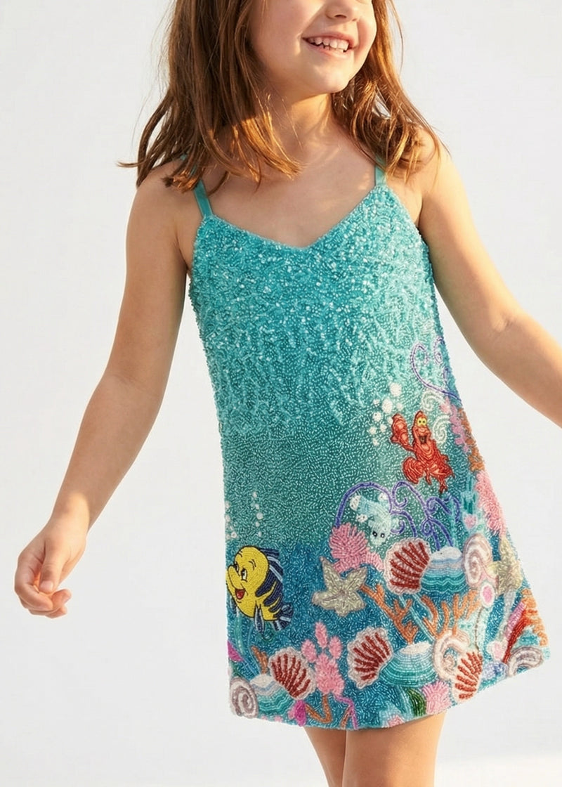 Child wearing a sequined dress with ocean-themed design on a white background