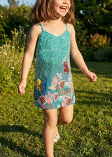 Child wearing a colorful dress with an underwater theme, standing in a grassy outdoor setting.