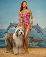 Woman in a pink swimsuit with a dog and dolphins in the background