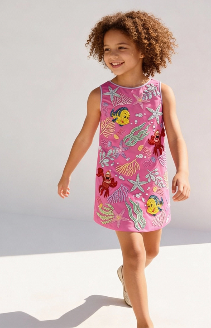 Child wearing a pink dress with undersea-themed graphics against a plain background